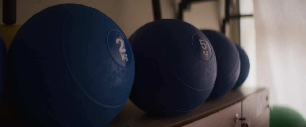 A close-up shot of blue medicine balls of various weights resting on a shelf in a modern gym