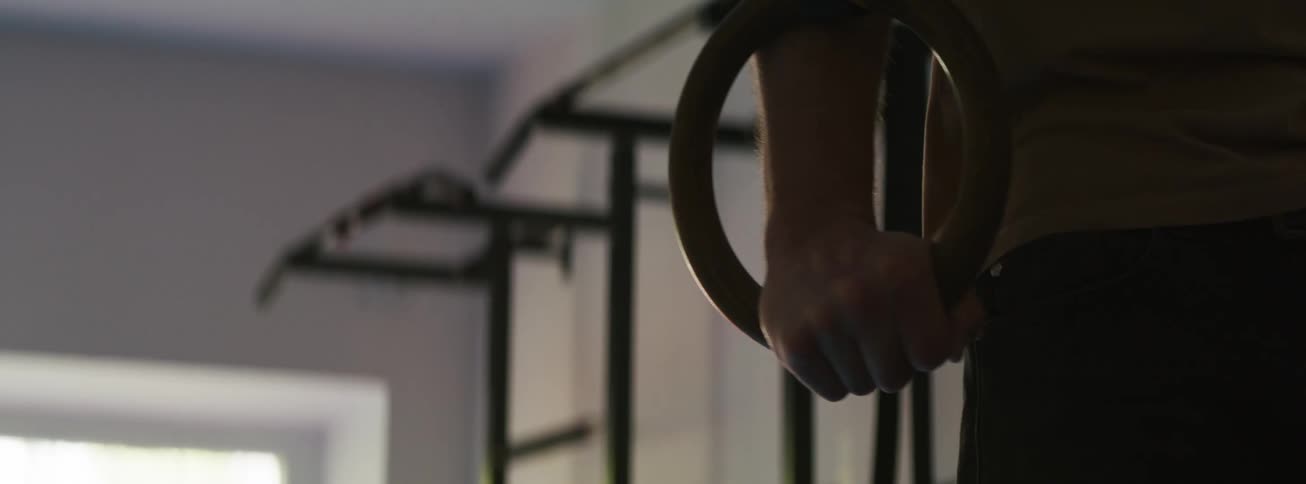 A slow-motion close-up shot captures an athlete's hand firmly gripping a wooden gymnastic ring in a dimly lit home gym