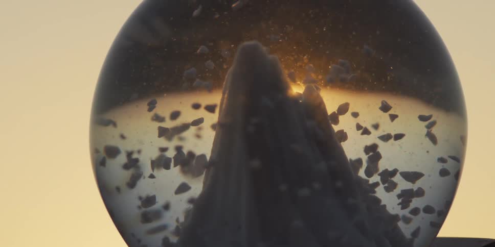 Sunset shines through a mountain snow globe as faux snow swirls in slow motion
