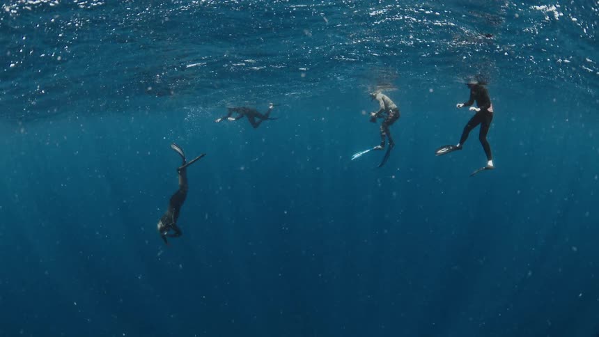 Underwater view of four freedivers floating on the surface of the vast, deep blue ocean in slow motion