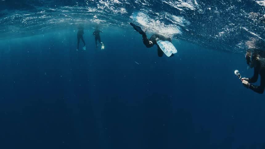 Slow motion underwater shot of a group of freedivers floating on the surface of the deep blue sea