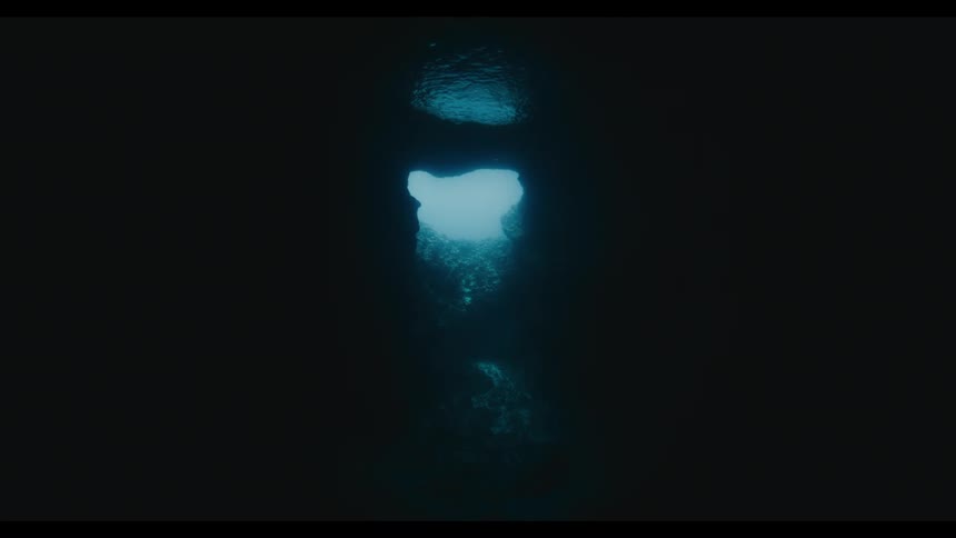 Sunlight penetrates the darkness of an underwater cave, creating a tranquil and mysterious view from the depths