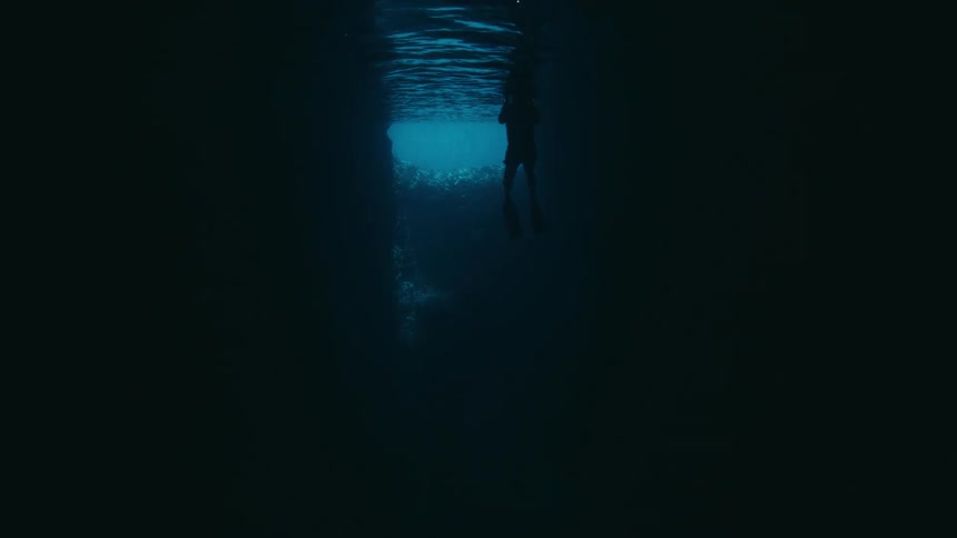 From the dark depths of an underwater cave, a snorkeler is silhouetted against the bright surface