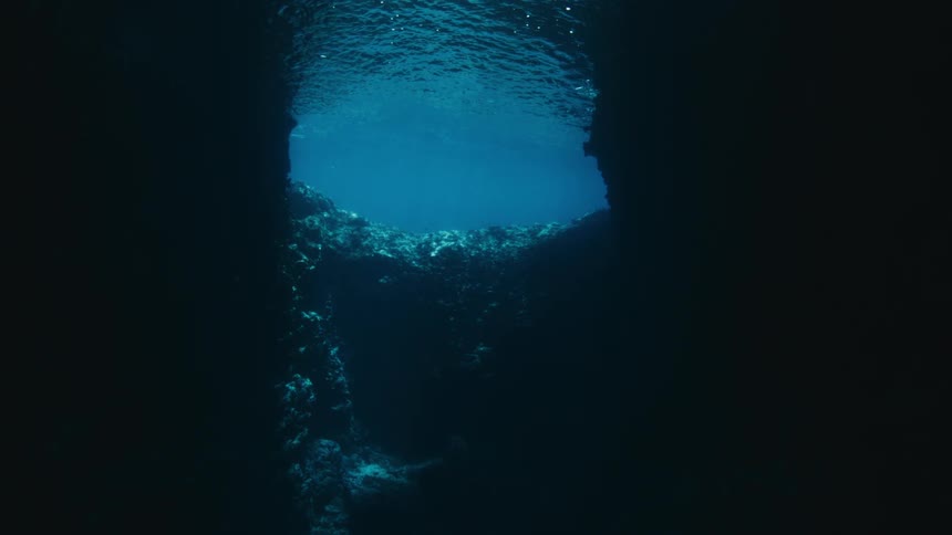 Serene underwater view from inside a dark cave, looking up at the bright blue ocean surface
