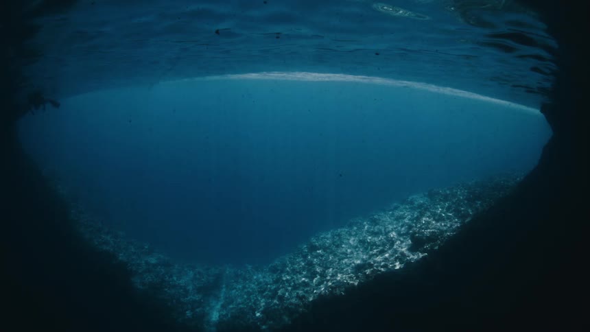 Ethereal underwater view from inside a grotto, looking up towards the sunlit surface and a distant diver