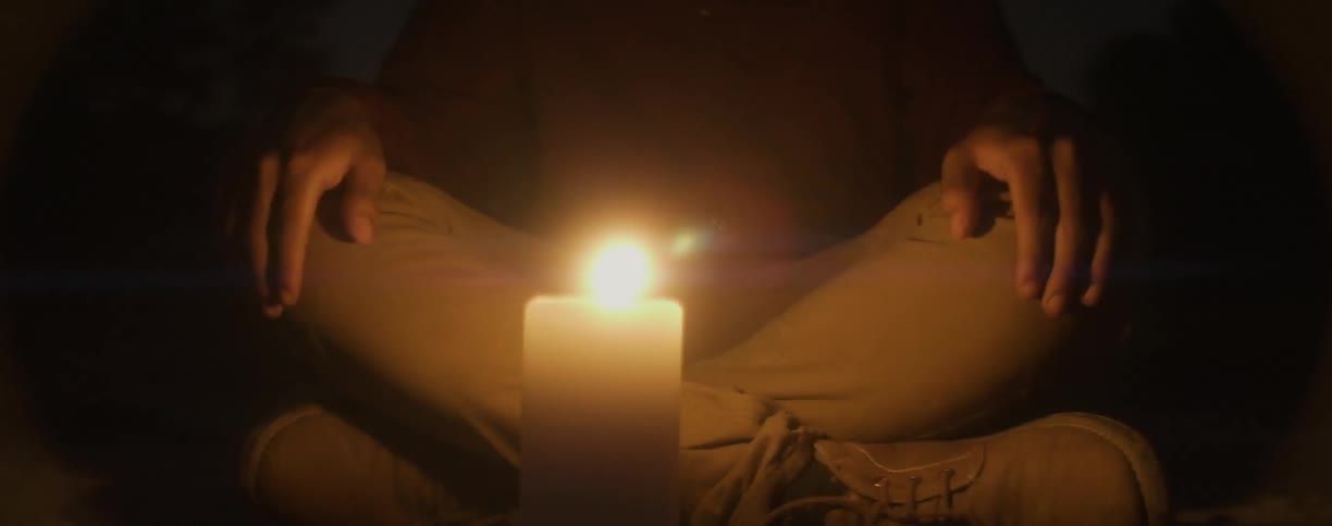 A person is sitting in the dark by a flickering candle