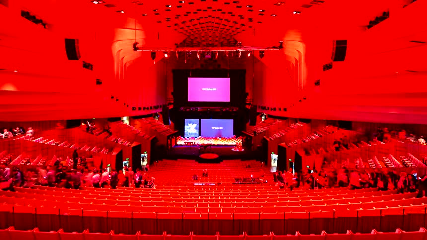 Time-lapse captures a massive crowd exiting a modern concert hall after an event, with the entire venue dramatically lit in red
