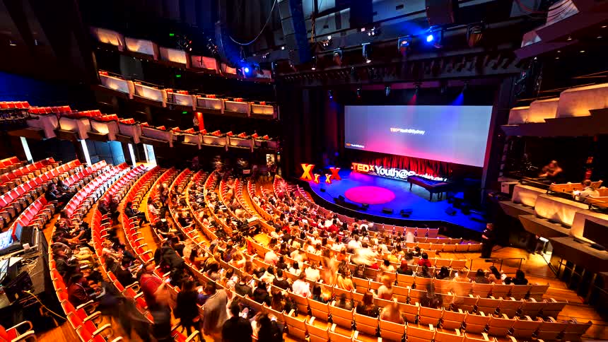 A time-lapse from a high angle shows an audience filling the seats of a large, modern auditorium before a TEDx Youth conference