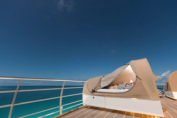 A man sleeps in a swag on the deck of a boat as the stars and clouds move across the night sky in this peaceful timelapse