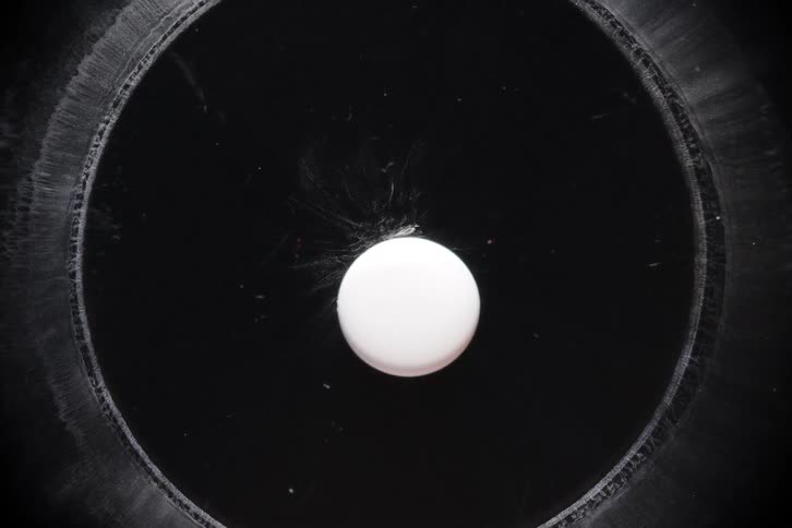Abstract macro top-down shot of a white pill dissolving in a time-lapse, creating expanding rings and misty clouds on a black background