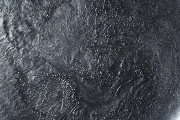 A mysterious, dark metallic liquid with a textured surface slowly undulates in a mesmerizing abstract background