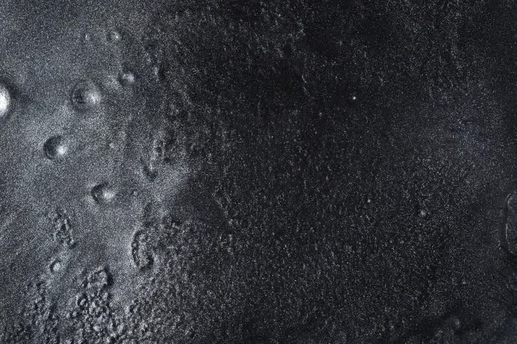 A top-down view of a mysterious, dark metallic surface slowly hardening and texturing