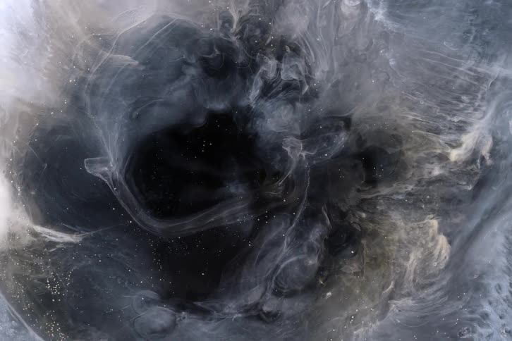 A mesmerizing abstract display as white and gold shimmering ink slowly billows and dissolves into a black liquid abyss