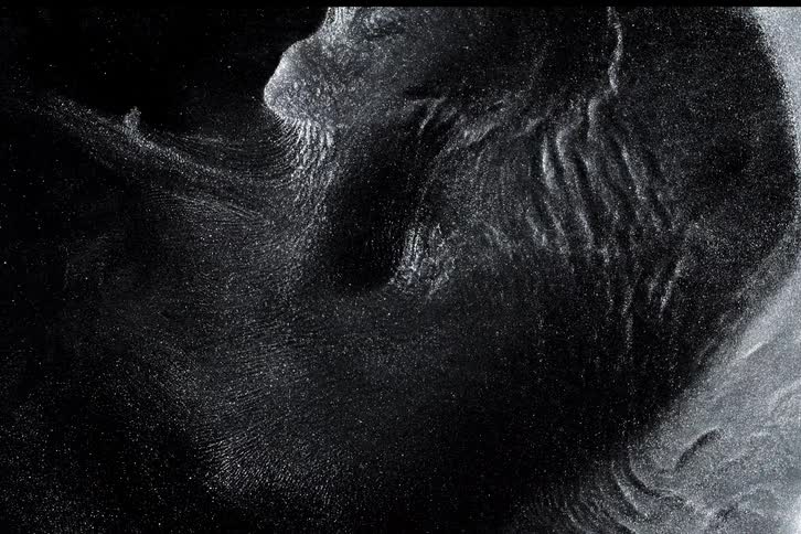 An abstract macro shot of shimmering silver particles slowly swirling in a dark liquid