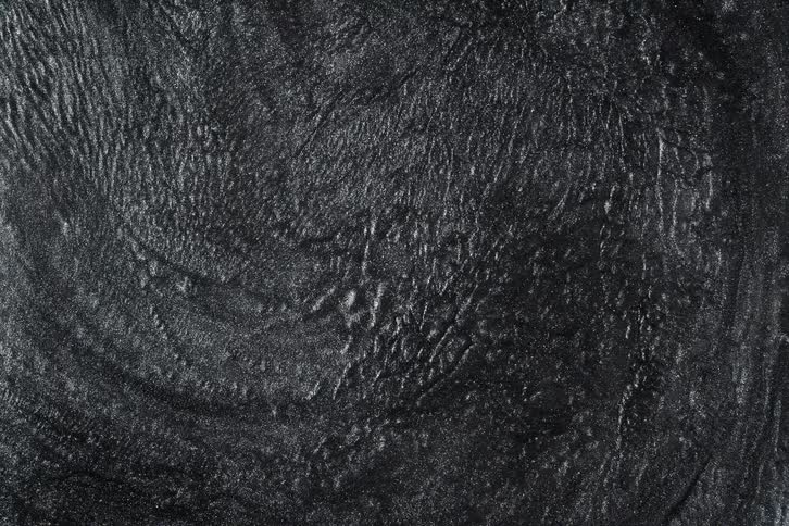 A dark, textured, and shimmering metallic liquid slowly stops moving in an abstract top-down view