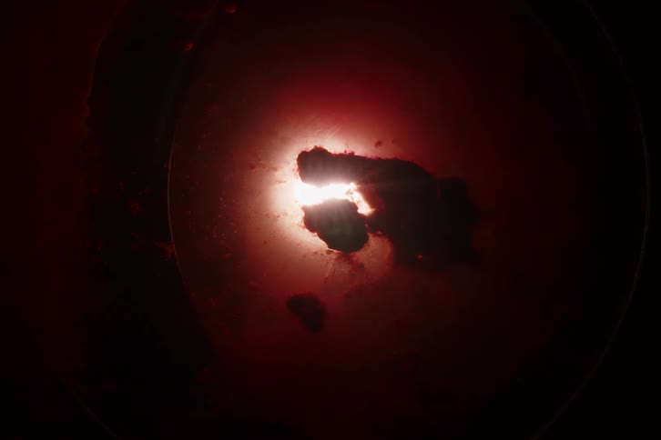 An abstract macro shot of dark particles suspended in a red liquid with a bright light source creating an ominous, celestial effect