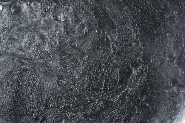 Dark, viscous, glittery metallic fluid slowly swirls, creating an abstract and textured background