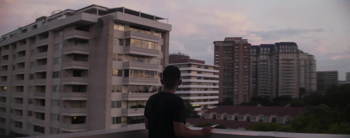 Man stands out on balcony looking out at buildings