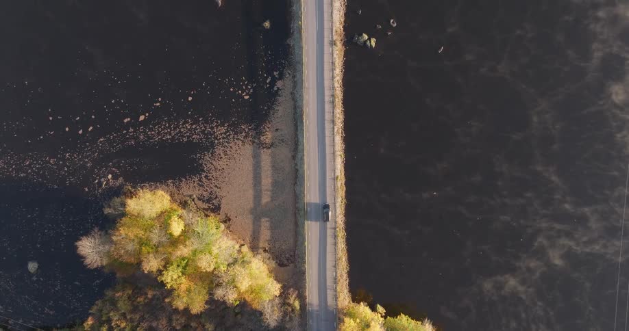 A top-down aerial view of a car driving along a scenic causeway through a misty lake during a beautiful autumn morning