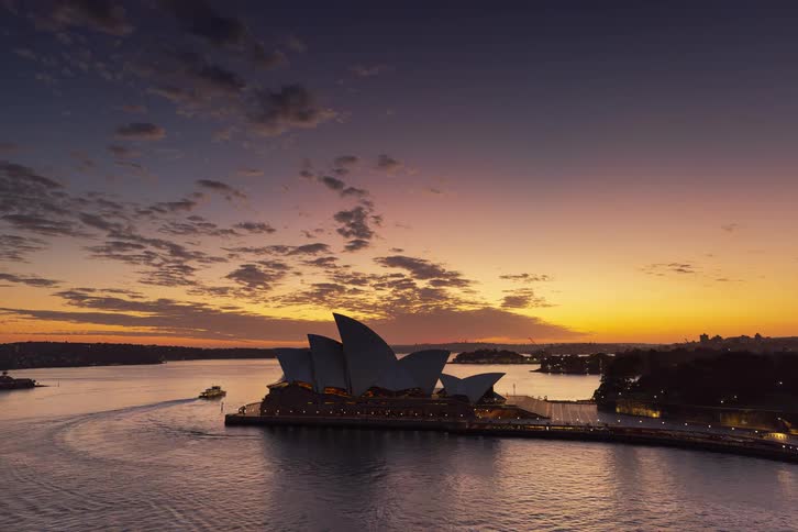 A beautiful time-lapse of the iconic Sydney Opera House transitioning from night to a dramatic and colorful sunrise over the harbor