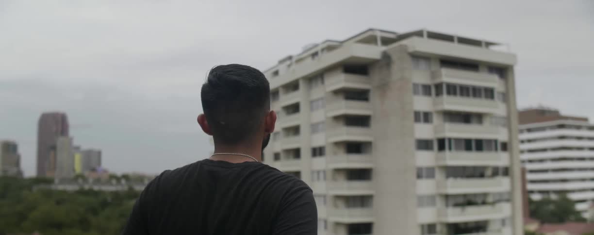 A man stands on a rooftop overlooking a city