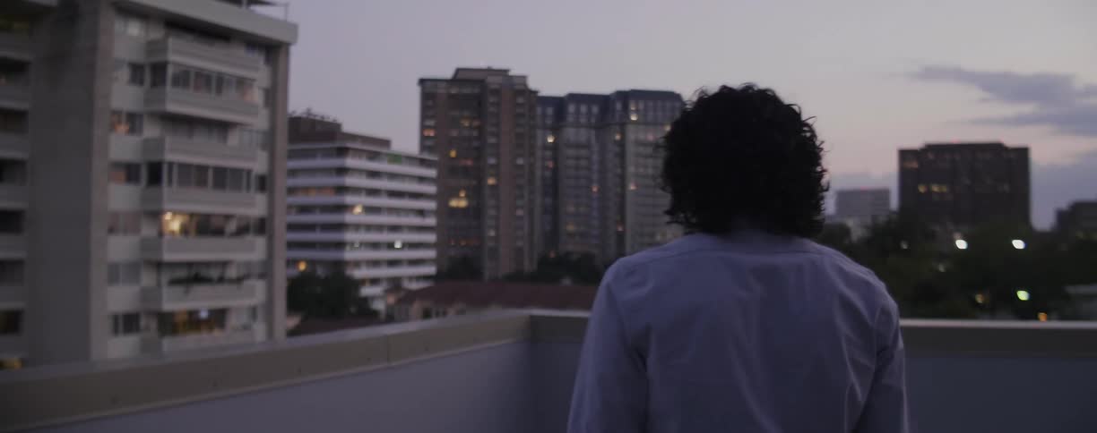 A young man is walking out on a rooftop in an urban area