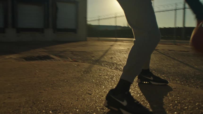 A young man skillfully dribbles a basketball in a gritty urban lot during a golden hour sunset