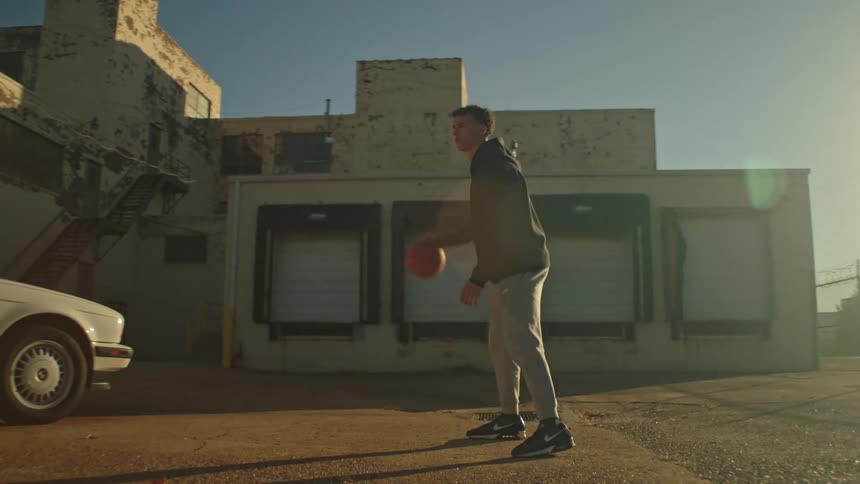 A young man practices his basketball dribbling skills in a gritty urban lot at sunset