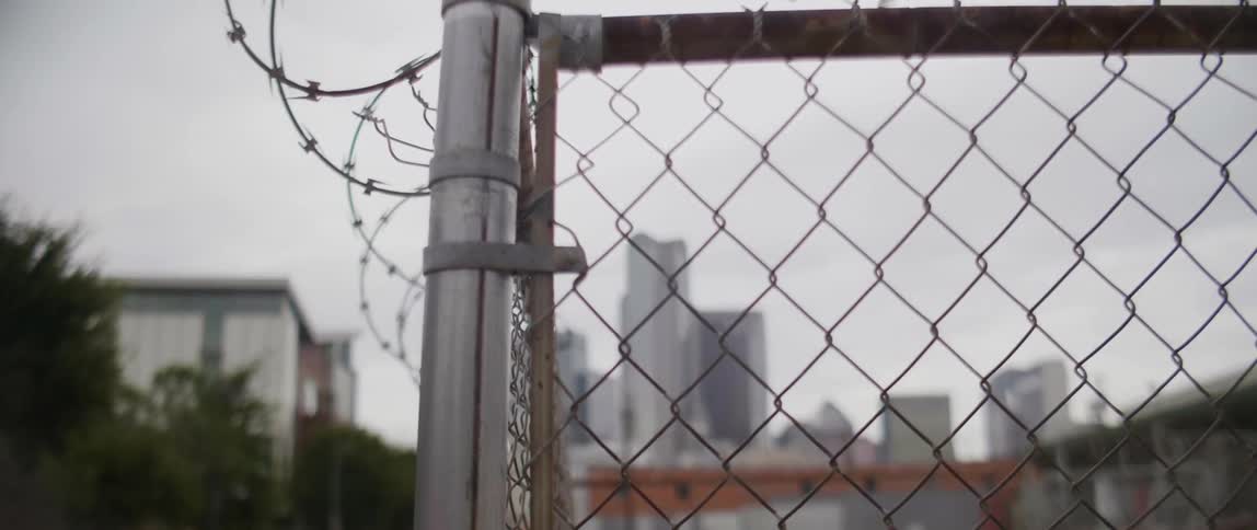 Barbed wire sitting on top of the chain link fence looking towards  the city skyline