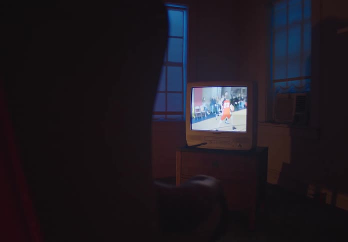 A person sits in a dark room at night watching a basketball game on an old, retro-style CRT television