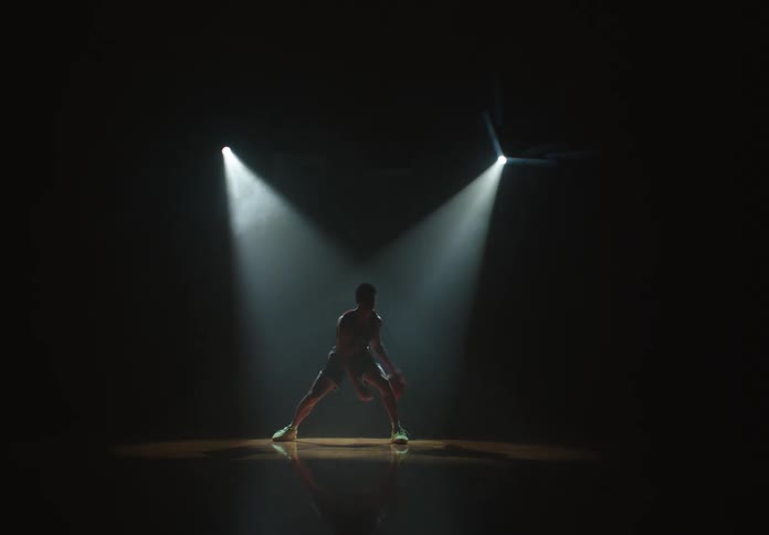Dramatic shot of a basketball player practicing dribbling moves alone on a dark court under two spotlights
