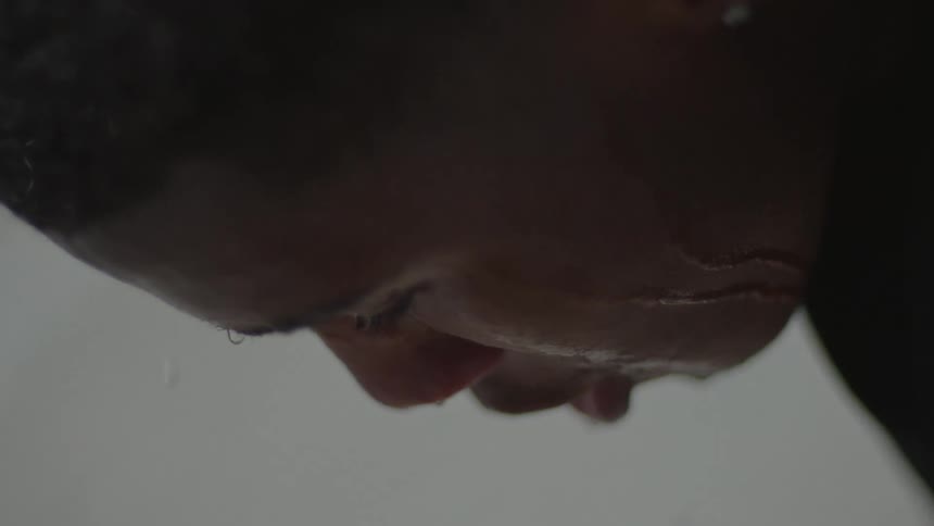 A dramatic slow-motion close-up of raindrops falling from a person's face