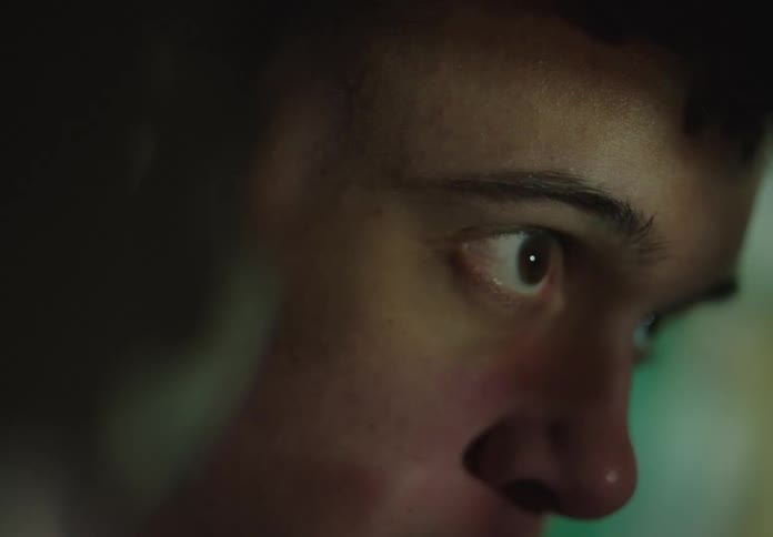 Close-up of a teenager's eye wide with focus while watching something on a screen in a dark room with flashing lights
