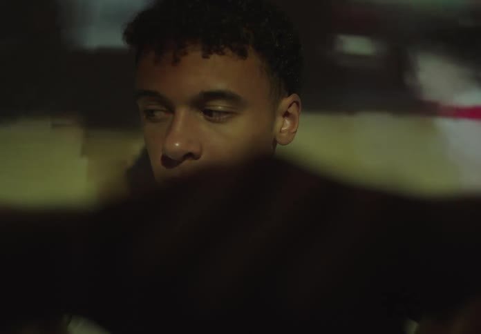 Close-up of a contemplative, bruised young man watching flashbacks of basketball games projected onto his face