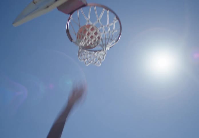 Dynamic shot of a basketball player scoring a layup on an outdoor court under the bright summer sun