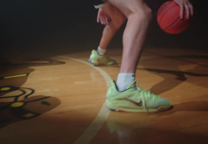 A focused basketball player intensely practices dribbling skills on a dark, spotlit indoor court