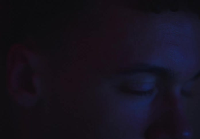 A man's eye reflects the glow of a screen at night as he watches intently