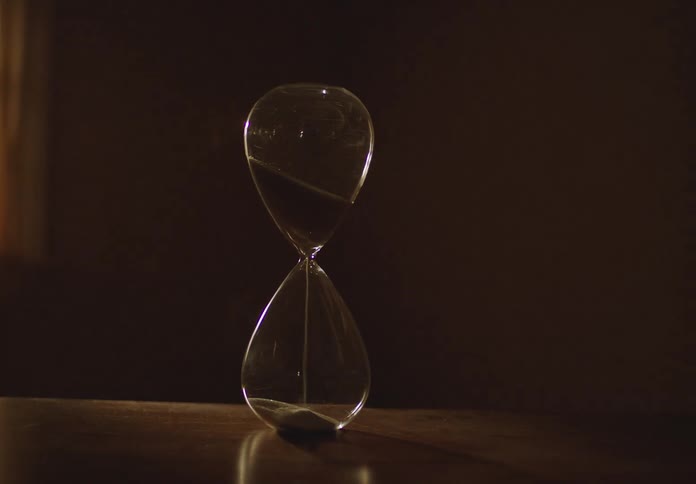 A slow zoom on an hourglass as its sand runs out on a wooden table while daylight fades to darkness in the background