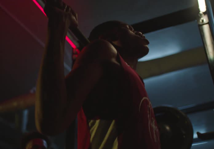 An athletic man grimaces with effort as he completes a heavy barbell squat in a dramatically lit weight room