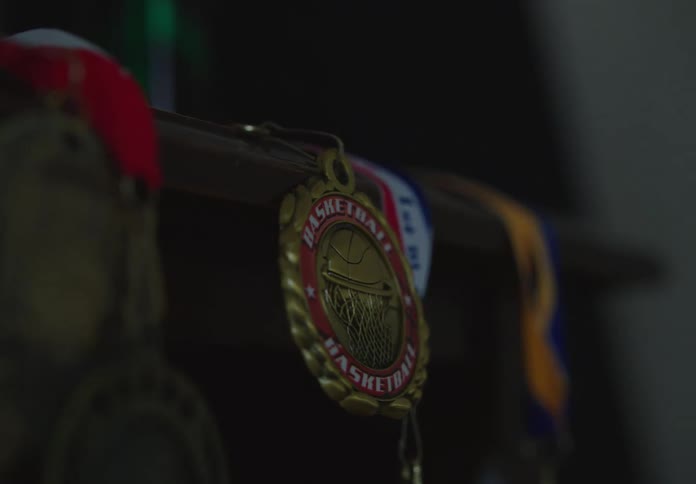 A dramatic rack focus shot reveals a collection of hanging basketball medals in a dark room