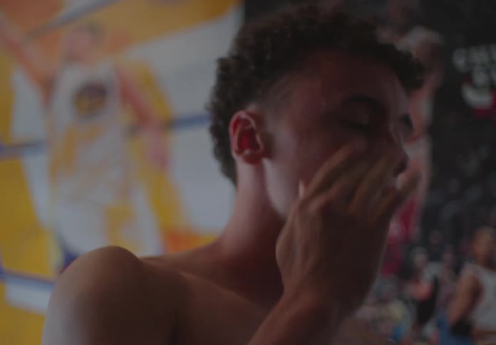 A thoughtful young man rubs his tired eyes in his dimly lit bedroom with basketball posters on the wall