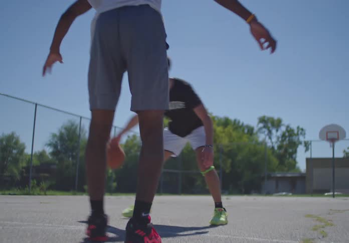 Low angle footage of young men playing basketball one on one on an outdoor court, ending with a successful layup