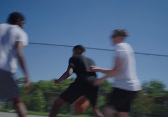 A young man dribbles past defenders and makes a successful jump shot during a pickup basketball game