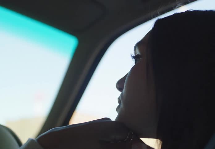 A thoughtful woman's profile is silhouetted as she drives her car from the dark into the bright light of day