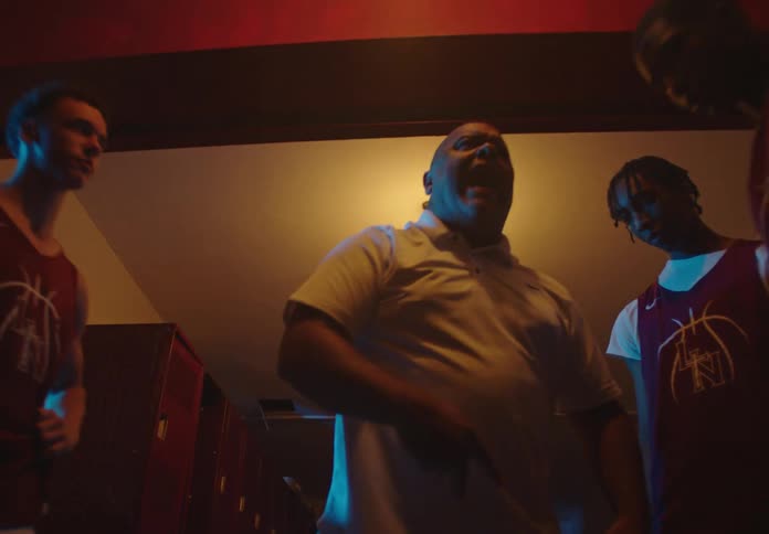A passionate basketball coach delivers an intense and motivational speech to his team in a dimly lit locker room