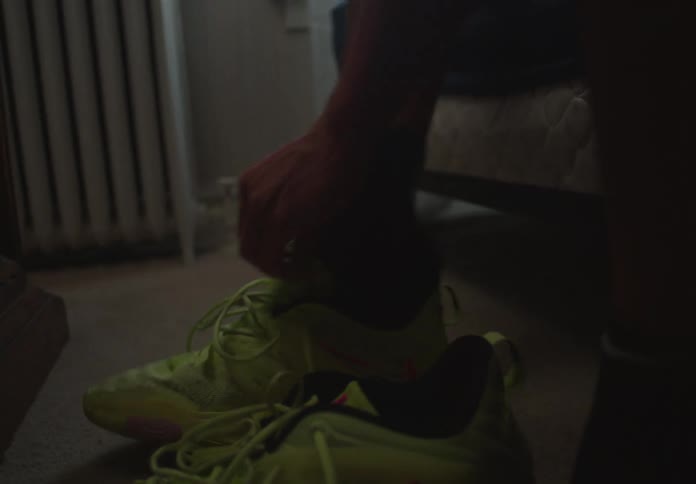 A young basketball player gets ready in his bedroom, lacing up his bright yellow sneakers
