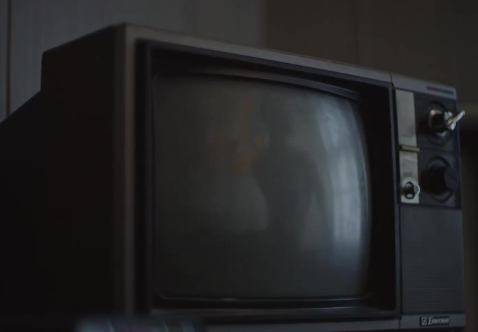 A slow, moody zoom into the screen of a vintage television set in a dark room