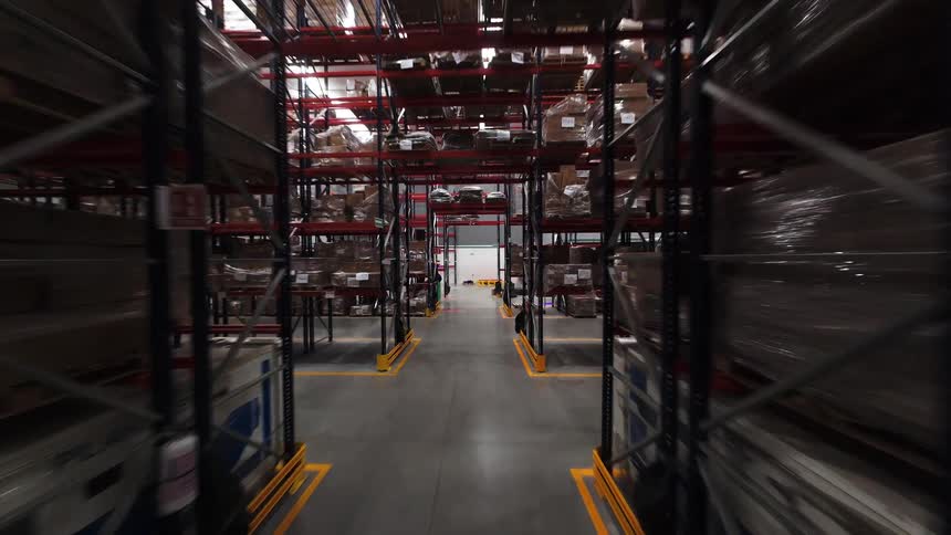 A smooth reverse dolly shot flies through a vast warehouse aisle, showcasing towering shelves packed with inventory and ending near a forklift operator