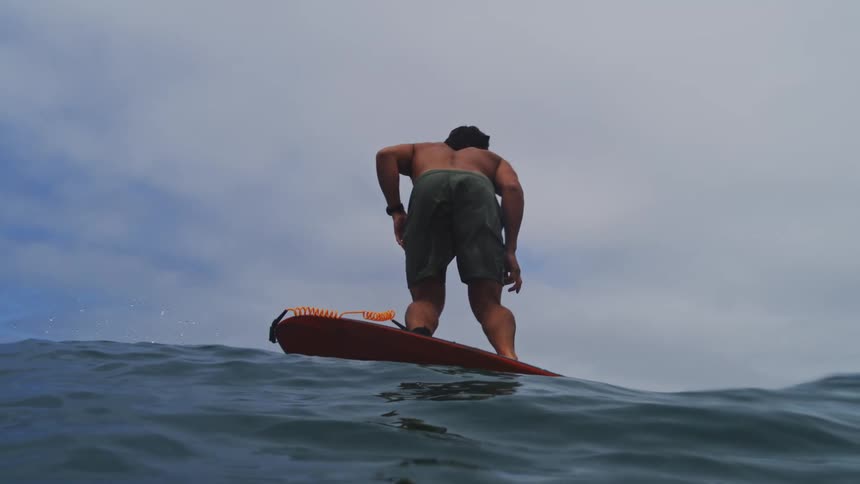 A man with long hair skillfully rides a hydrofoil surfboard, gliding effortlessly above the ocean waves in dramatic slow motion
