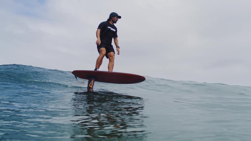 A man skillfully rides a hydrofoil surfboard on a gentle ocean wave in a stunning slow-motion water-level shot
